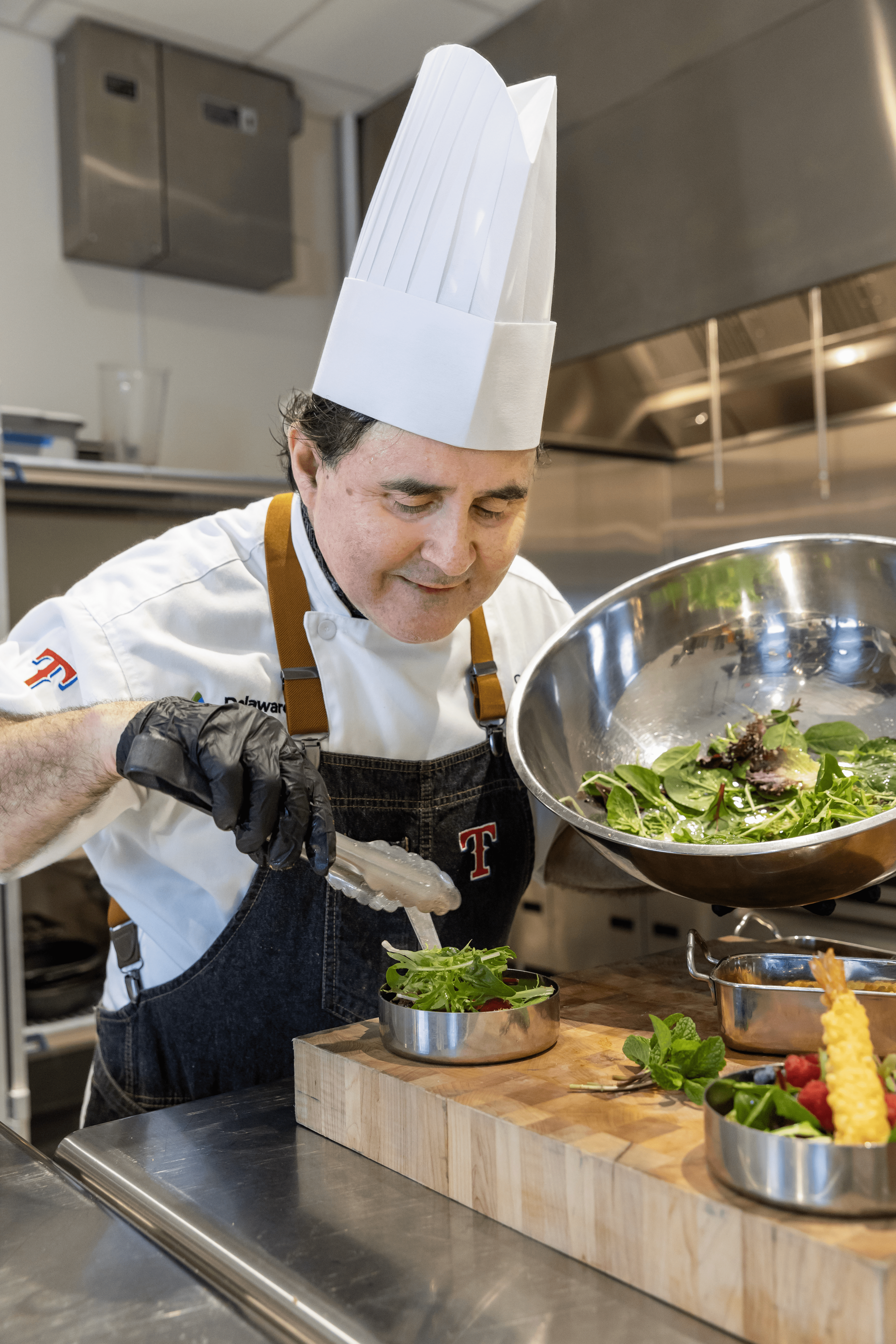 Chef transferring salad leaves from bowl into pan